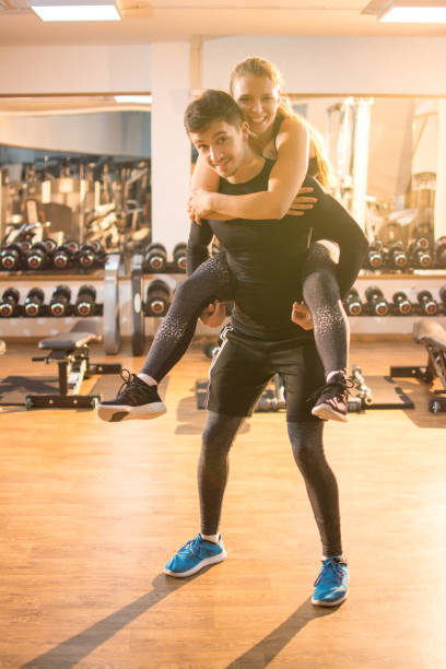 istock Young handsome man carrying his girlfriend on his back in gym. 928996430