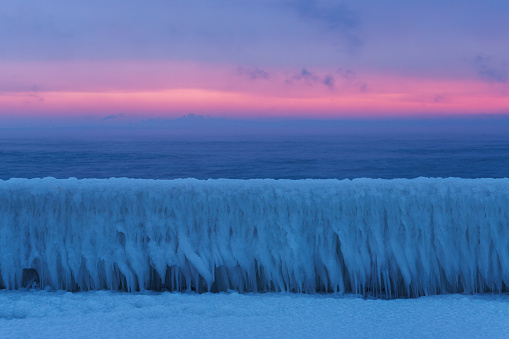 Winter sea landscape with frozen obstruction in icicles at morning dawn.