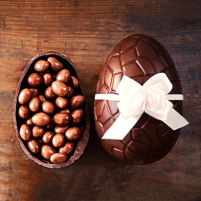 Chocolate Easter Eggs on Wooden Background with color ribbon bow and broken egg with chocolate candies.