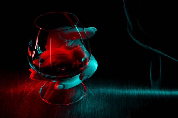 A glass of cognac in hand on dark background. Red and green lights.