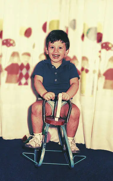 vintage color image of a happy kid looking at camera while riding a horse toy at home.