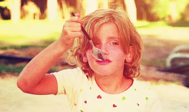 Vintage toned image of a girl eating ice cream with a spoon.