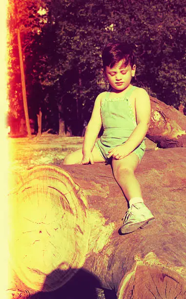 vintage and burnt color image of a toddler sitting on a cut tree trunk.