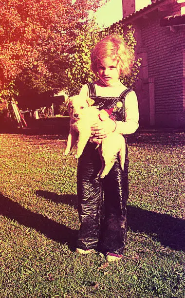 Vintage toned image of a girl outdoors in front of the camera and holding a puppy.