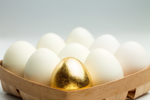 One golden egg among white eggs in a wooden box.