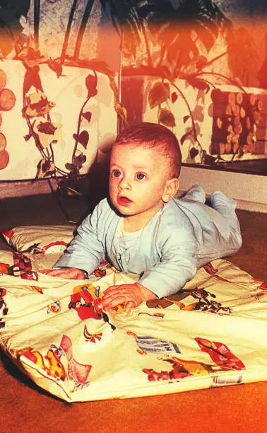 vintage color image of a cute baby boy laying on floor and looking up.