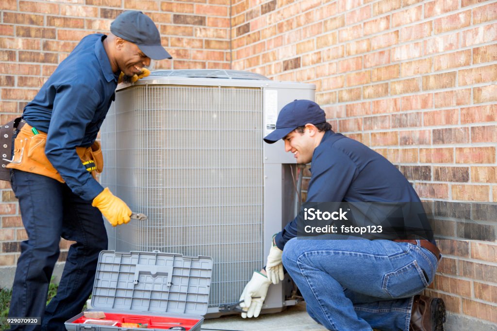 Multi-ethnic team of blue collar air conditioner repairmen at work. Multi-ethnic team of blue collar air conditioner repairmen at work.  They prepare to begin work by gathering appropriate tools from their tool box. Air Conditioner Stock Photo