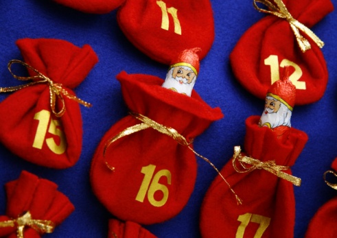 Christmas gifts in craft packaging and canvas bags with numbers on red paper, a fir branch with a garland, an Advent calendar on the background of boards made of old wood