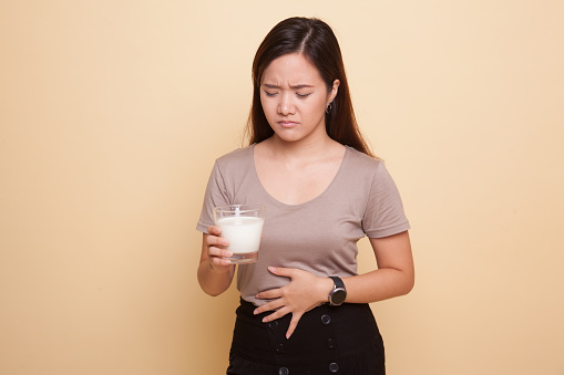 Asian woman drinking a glass of milk got stomachache on beige background