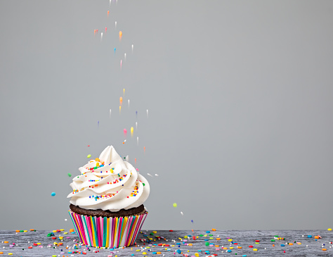 A Cupcake being decorated with colorful Sprinkles.