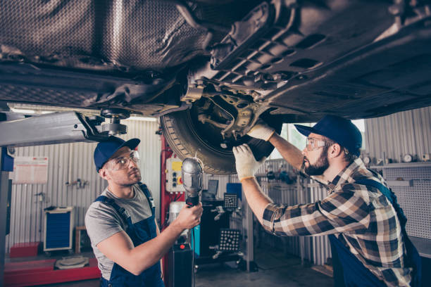 engineering, protection, reliability, safety, oneness, colleagues, assistance. professionals in blue overalls, protective spectacles are examining changing tires, tyres, brake pads at work shop - automotive accessories imagens e fotografias de stock