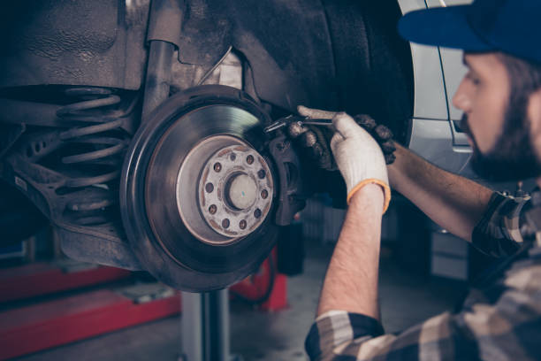 side profile close up shot of expert specialist technician changes tires, tyres or brake pads of lifted up car, at auto workshop, wears checkered shirt, uniform costume, hat headwear - travão imagens e fotografias de stock