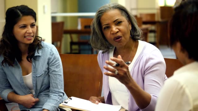 Beautiful senior African American college professor meets with a group of students pursuing an advanced degree. She gestures while explaining something to the students.