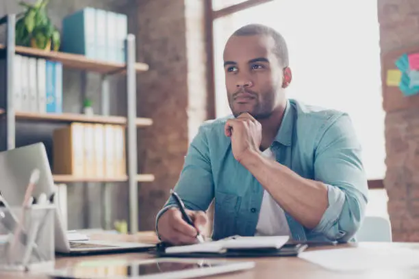 Photo of Skeptic, unsure, uncertain, doubts concept. Young african student is making decision sitting at the office in casual smart