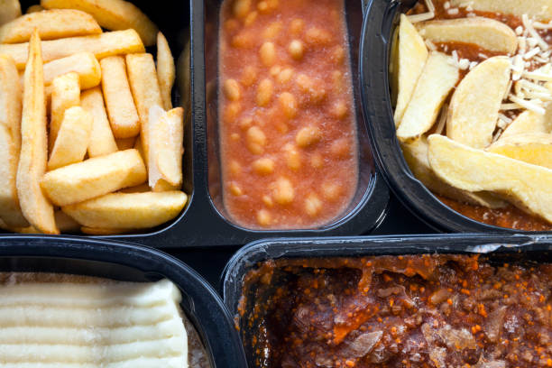 Microwaveable, ready to eat meals of chips, mince,beans, lasagna, in black plastic boxes, still unfrozen . Selection of frozen, processed, ready made foods, consisting of potato chips, mince, lasagna in black, plastic containers . Microwave meals ready to heat up . Ready To Eat stock pictures, royalty-free photos & images