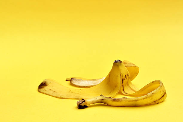 buccia di banana su sfondo giallo - slapstick foto e immagini stock