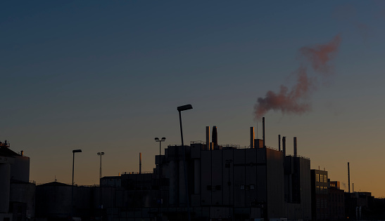 A factory outline with smoke pumping, silhouetted at sunset