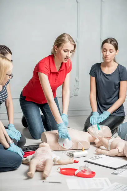Young woman instructor clinging contacts on a dummy teaching how to make defibrillation during the first aid group training indoors