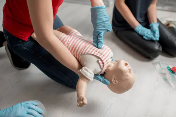 Woman instructor showing how to make chest compressions on a baby dummy during the first aid group training indoors