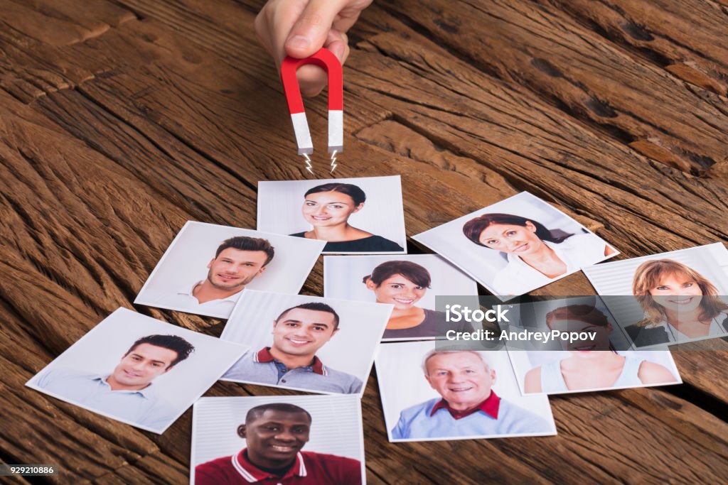 Businessperson's Hand With Horseshoe Magnet Attracting People Close-up Of A Businessperson's Hand With Horseshoe Magnet Attracting Photograph Of Smiling People Love At First Sight Stock Photo