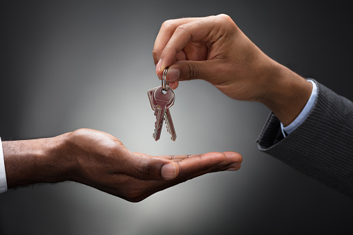 Close-up Of Hands Giving Keys Of An Apartment Against Gray Background