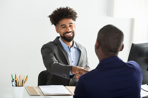 Smiling Young Businessman Shaking Hand With Male Candidate In Office