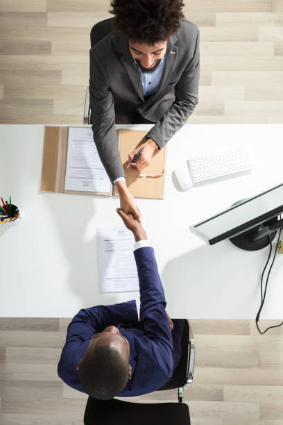 Young Businessman Shaking Hand With Candidate Over White Desk High Angle View Of Young Businessman Shaking Hand With Male Candidate Over White Desk interview event stock pictures, royalty-free photos & images