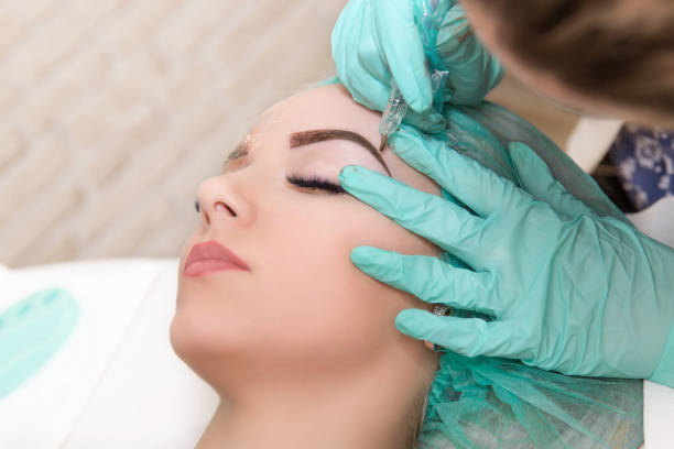 Microblading eyebrows work flow in a beauty salon. Woman having her eye brows tinted. Semi-permanent makeup for eyebrows. Focus on model's face and eyebrow
