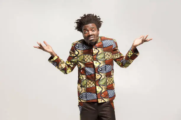 Confused afro man puzzled and say don't know, maybe. Indoor, isolated on gray background