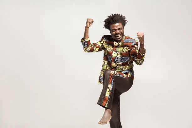 Yes! Expression happiness african man in traditional clothes rejoicing win. Indoor, isolated on gray background