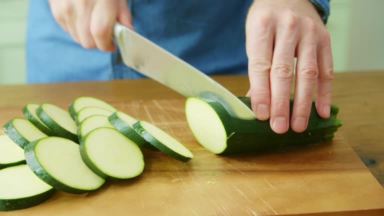 Man's Hands Slicing Fresh Zucchini With Knife On Cutting Board