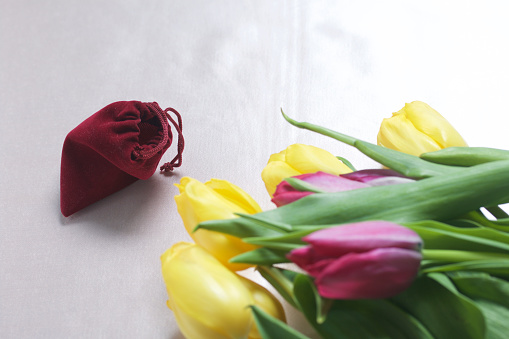 Gifts for loved ones. A bouquet of yellow and pink tulips is scattered on a light surface. Nearby is an open velvet bag of red color with gold jewelry.