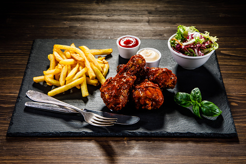 Roast chicken legs with French fries on wooden table