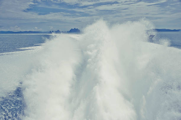 Prop wash spray (rooster tail) and wake trails from a high-speed motorboat and island background