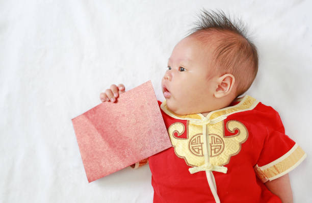 bébé garçon en cheongsam avec holding enveloppe rouge se trouvant sur fond de fourrure blanche. - asian culture dragon textile symbol photos et images de collection