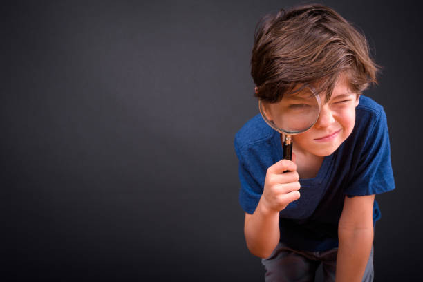портрет милый мальчик с помощью увеличительного стекла на черном фоне - searching child curiosity discovery стоковые фото и изображения
