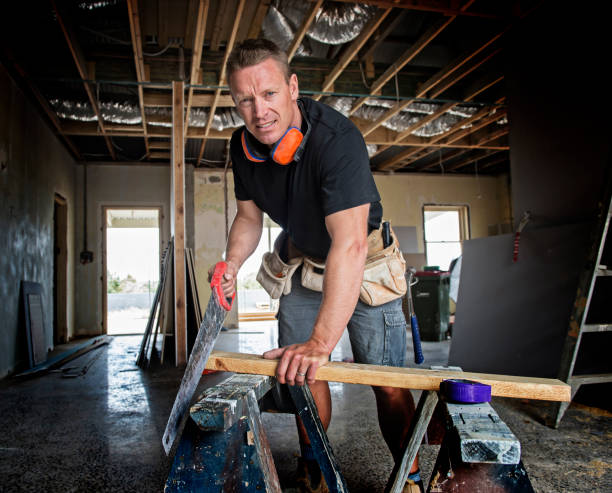 attractive and confident constructor carpenter or builder man working cutting wood with manual saw at industrial construction site in installation and renovation blue collar work industry