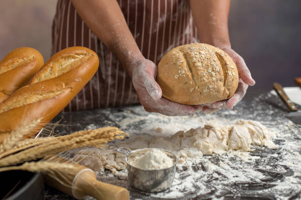 istock Chef holds the fresh bread in hand. Man preparing buns at table in kitchen 929485378