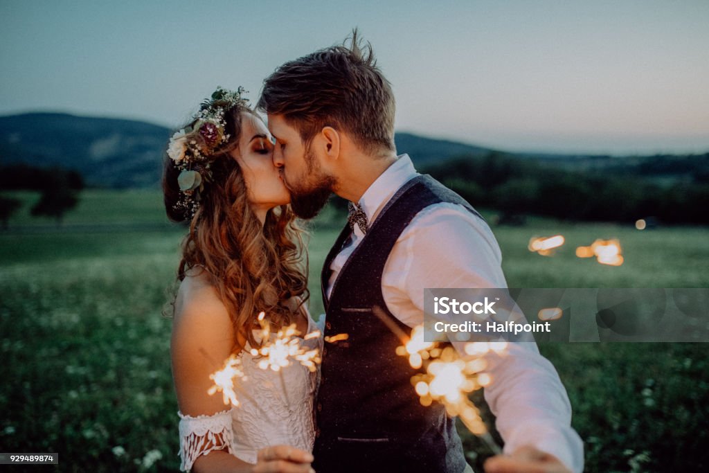 Beautiful bride and groom with sparklers on a meadow. Beautiful young bride and groom on a meadow in the evening, holding sparklers. Wedding Stock Photo