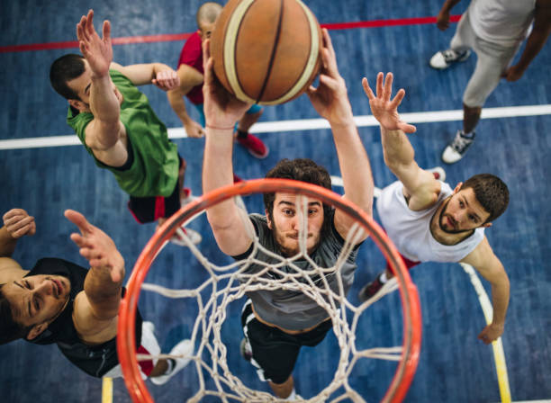 Slam dunk on a basketball court! High angle view of a determined basketball player slam dunking the ball while passing through defensive players. offense sporting position stock pictures, royalty-free photos & images