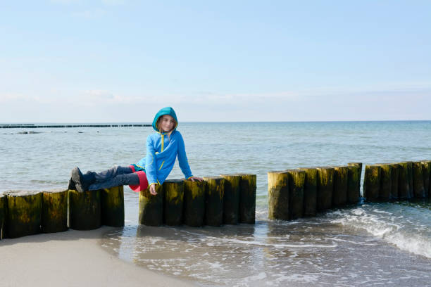 A 9-year-old Caucasian girl stands on a sandy beach and admires the seascape and sea waves.
