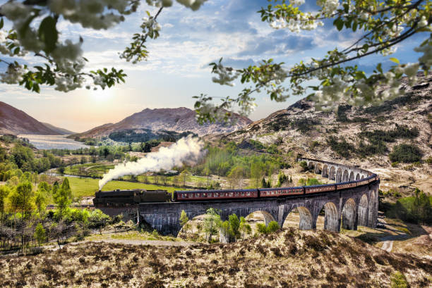 viadotto ferroviario di glenfinnan in scozia con il treno a vapore giacobita contro il tramonto sul lago - glenfinnan foto e immagini stock