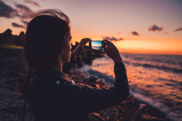 frau am strand den sonnenuntergang fotografieren - abenddämmerung fotos stock-fotos und bilder