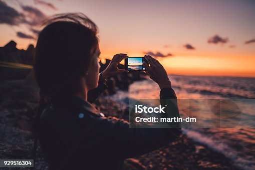 istock Woman at the beach photographing the sunset 929516304
