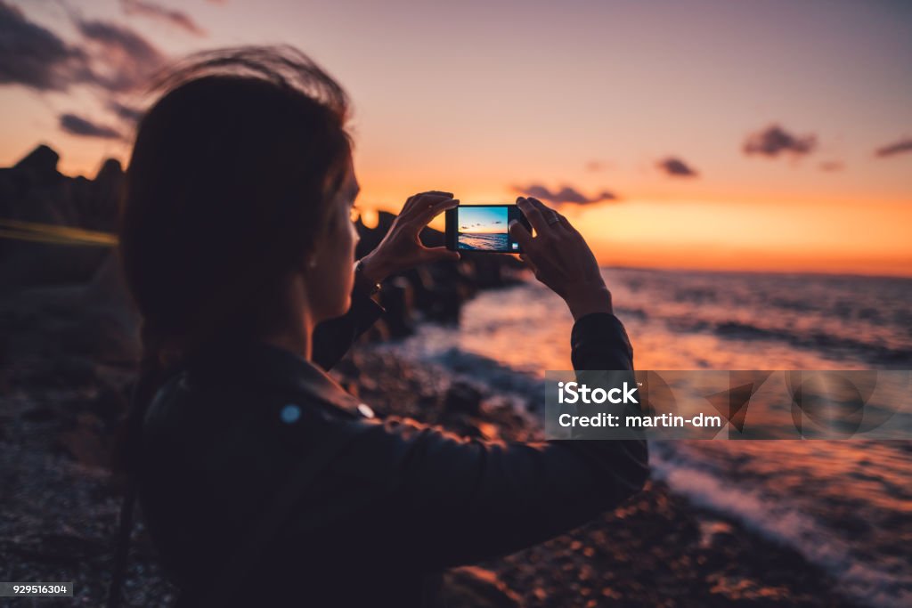 Woman at the beach photographing the sunset Woman on beach holiday taking photos with smartphone on sunset Photography Stock Photo