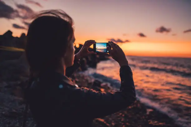 Woman on beach holiday taking photos with smartphone on sunset