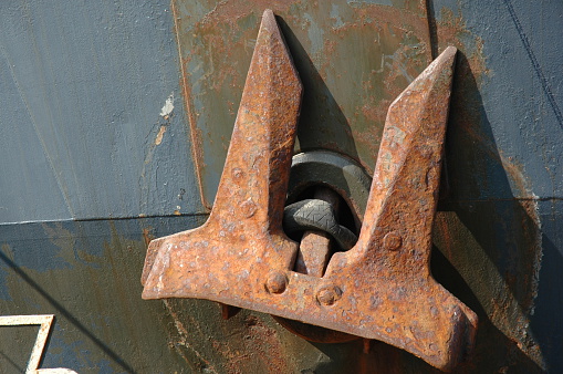 An old, rusting anchor on a large ship in dock.  The car tyre prevents damage from the anchor's movement to the hull of the ship. Leith Docks, Edinburgh, Scotland.