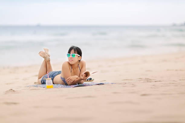 A young woman is relaxing and reading a book at the beach.