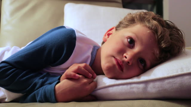Child layed in sofa watching screen. Candid 4K clip of young boy starring at TV screen at night