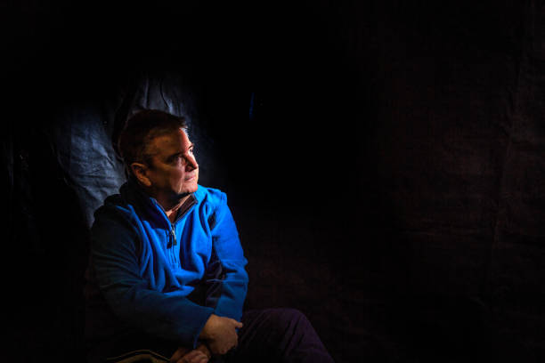 Senior man wearing blue sweater picked out by spotlight in dark room.